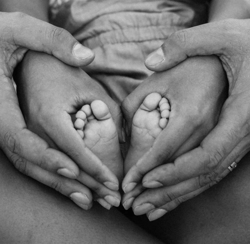 Une photographie en noir et blanc représentant des mains d'adultes entourant délicatement les pieds d'un enfant, symbolisant la protection, l'amour et le lien familial. Cette image évoque la douceur et la sécurité au sein de la famille, tout en mettant en lumière l'importance des relations intergénérationnelles et du soutien mutuel.