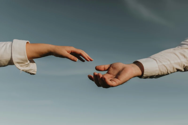 Deux mains tendues l'une vers l'autre, symbolisant la connexion, le soutien et l'accompagnement. Le ciel dégagé en arrière-plan évoque un sentiment de sérénité et d'ouverture.